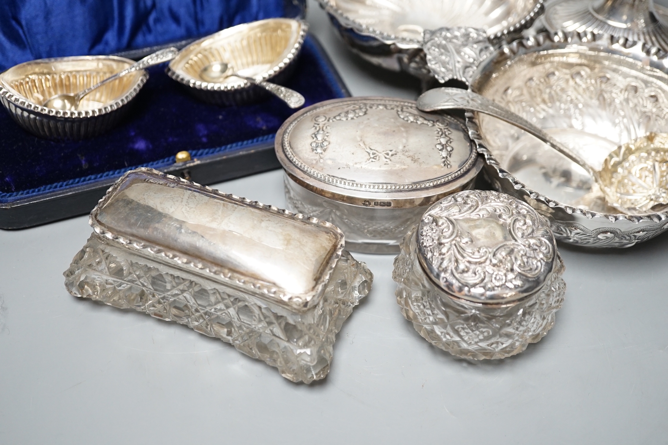 A Victorian repousse silver two handed bowl, one other silver bowl, a silver sifter spoon, four silver mounted glass toilet jars, a silver dwarf candlestick and a cased pair of silver salts.